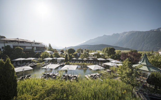 Der Naturbadesee des Alpenresort Schwarz mit Liegen und Sonnenschirmen vor den Bergen.