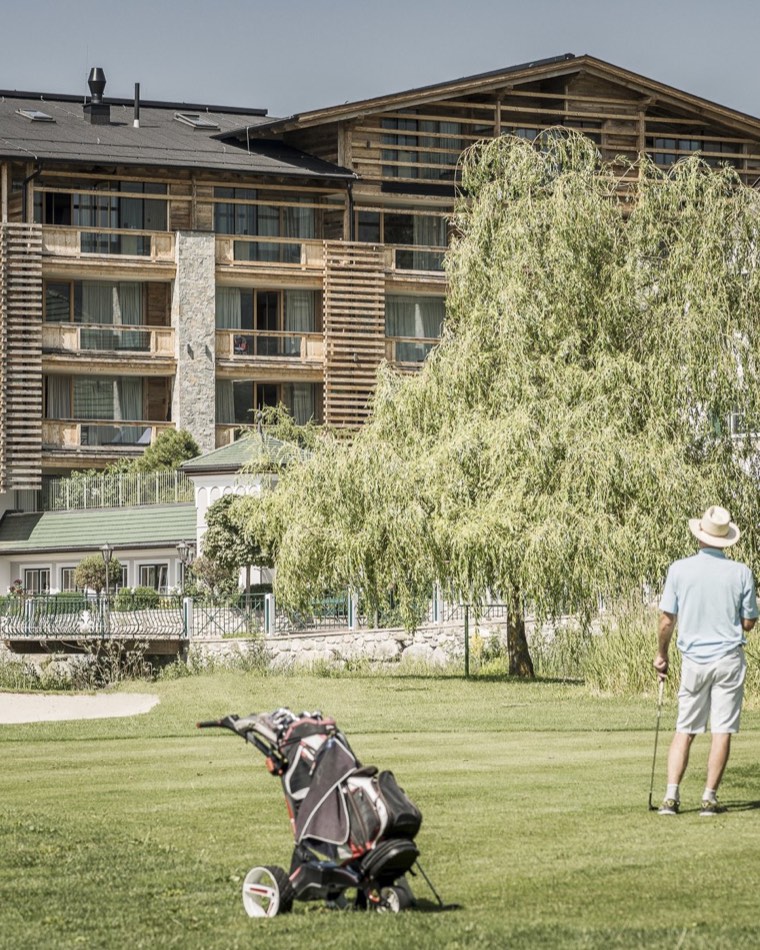 Golfer auf dem Übungsgrün, dahinter die Holzfassade des Alpenresort Schwarz.