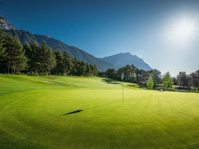 Ein Grün der Championcourse mit Fahne im Gegenlicht, links die Mieminger Kette.
