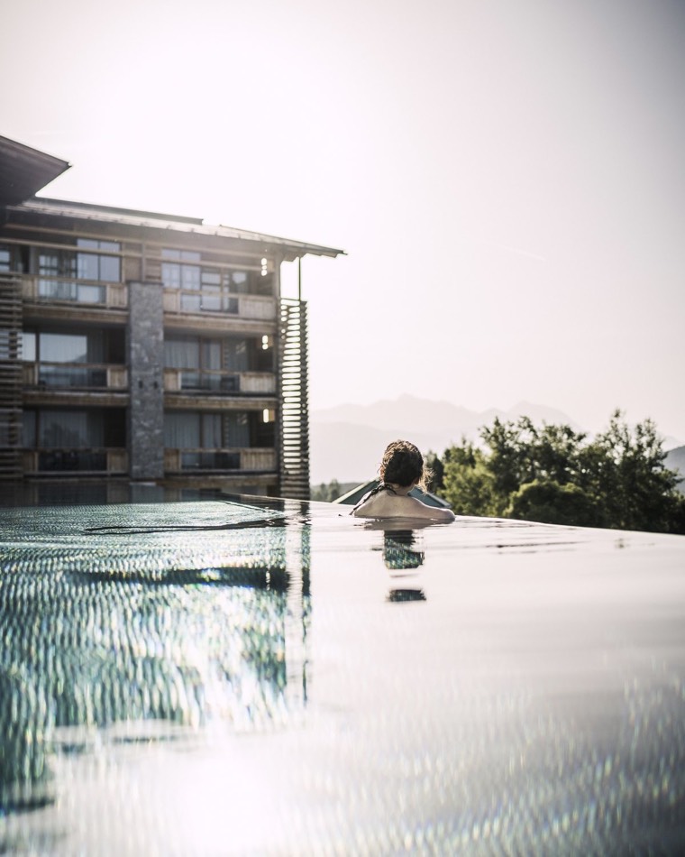 Eine Frau im Infinity-Pool des Alpenresort Schwarz blickt auf die Berge.