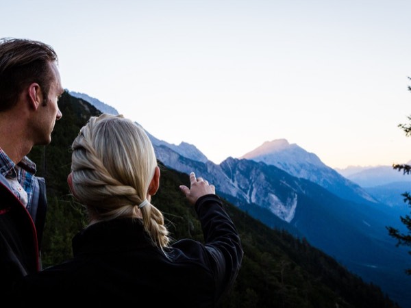 Zwei Personen blicken beim Sonnenaufgang über die Tiroler Alpen.
